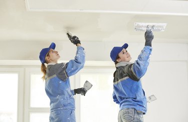 female plasterer painter at indoor ceiling renovation decoration stopping with spatula and plaster