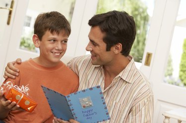 Father holding card by son  (10-12) holding present, smiling