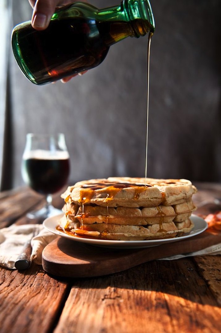 Maple syrup being drizzled over a stack of waffles.