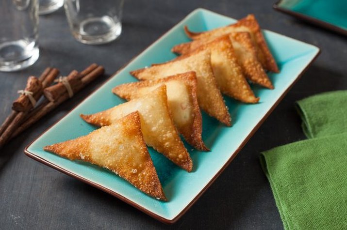 Golden brown cream cheese wontons stacked together on a plate.