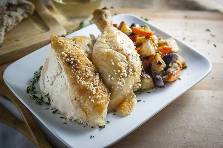 A freshly baked chicken served with a generous serving of roasted veggies.