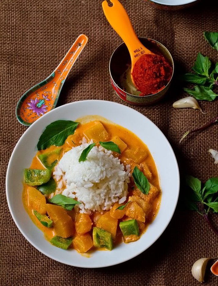 Thai pumpkin curry with green bell peppers and fresh basil leaves, and a scoop of steamed rice.