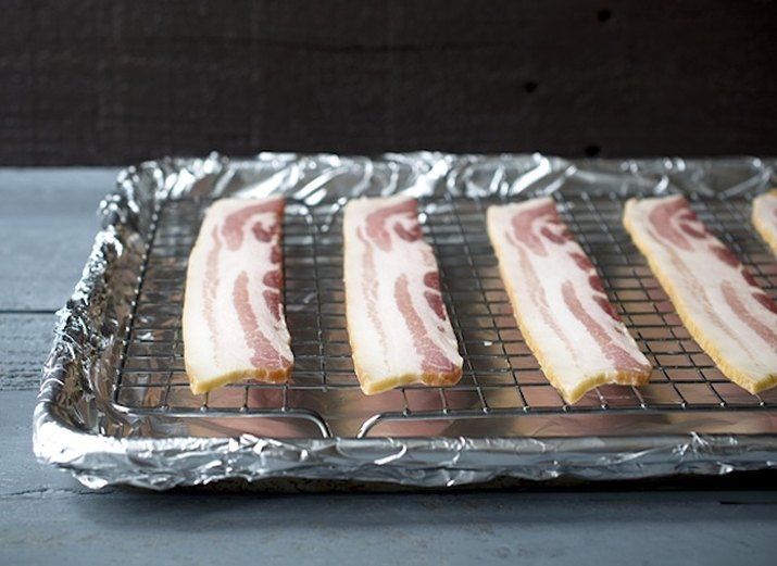 Raw bacon spaced evenly on wire rack atop baking sheet.
