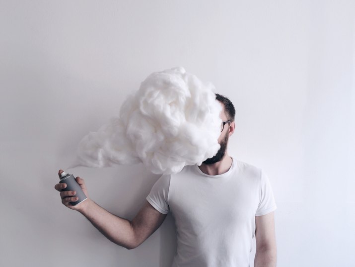 Man Spraying Shaving Cream In Front Of Face Against Wall